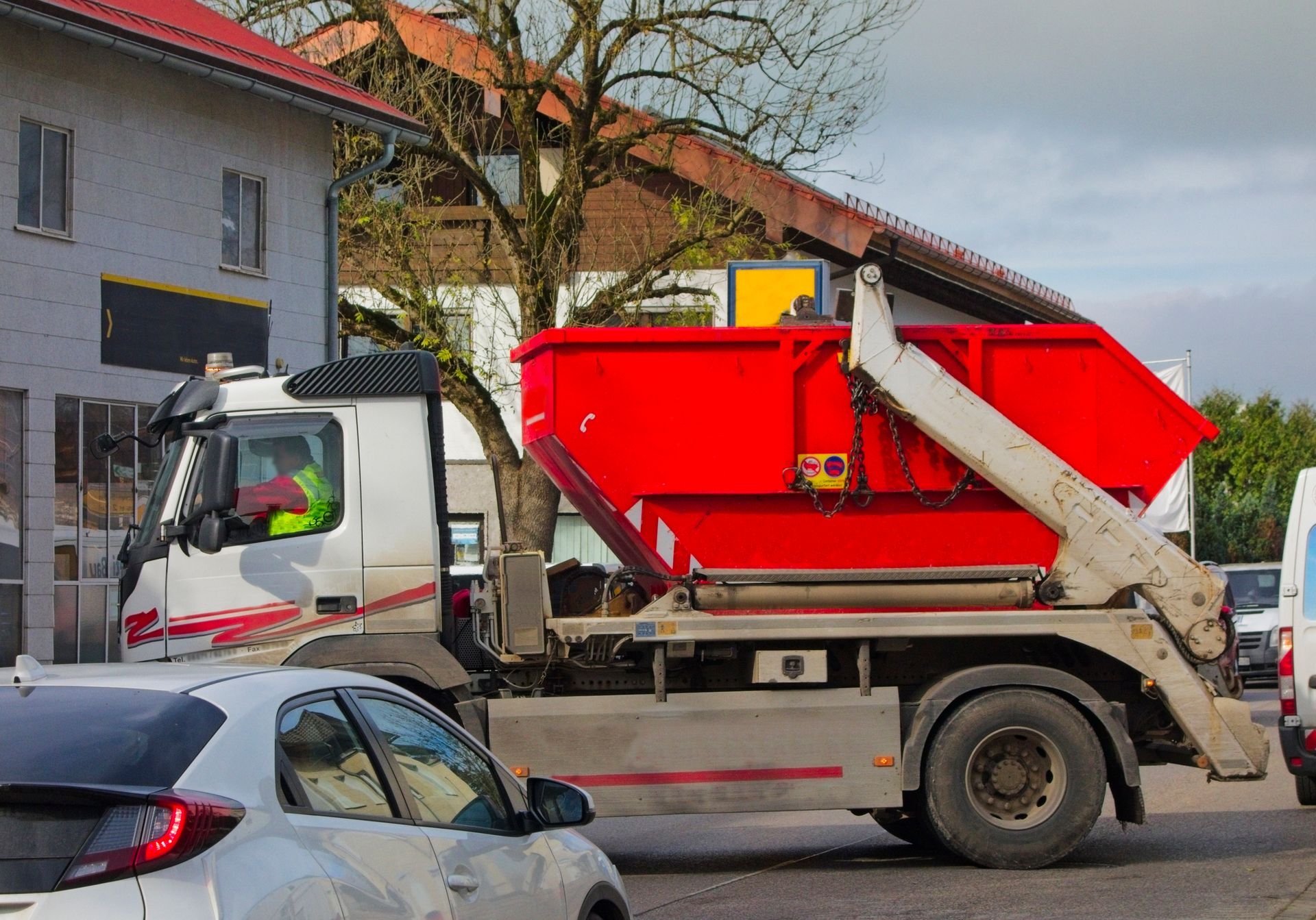 A garbage truck is parked in front of a building, carrying a large garbage bin in its truck bed.