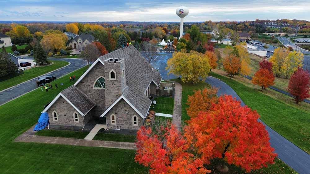 Church in autumn with colorful trees, green grass, and a water tower in the background.
