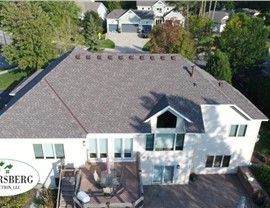 Aerial view of a white two-story house with a brown shingle roof and a deck.