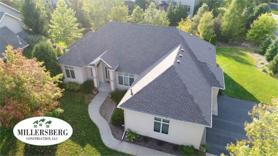 Aerial view of a cream-colored house with a dark gray roof, surrounded by green trees and grass.