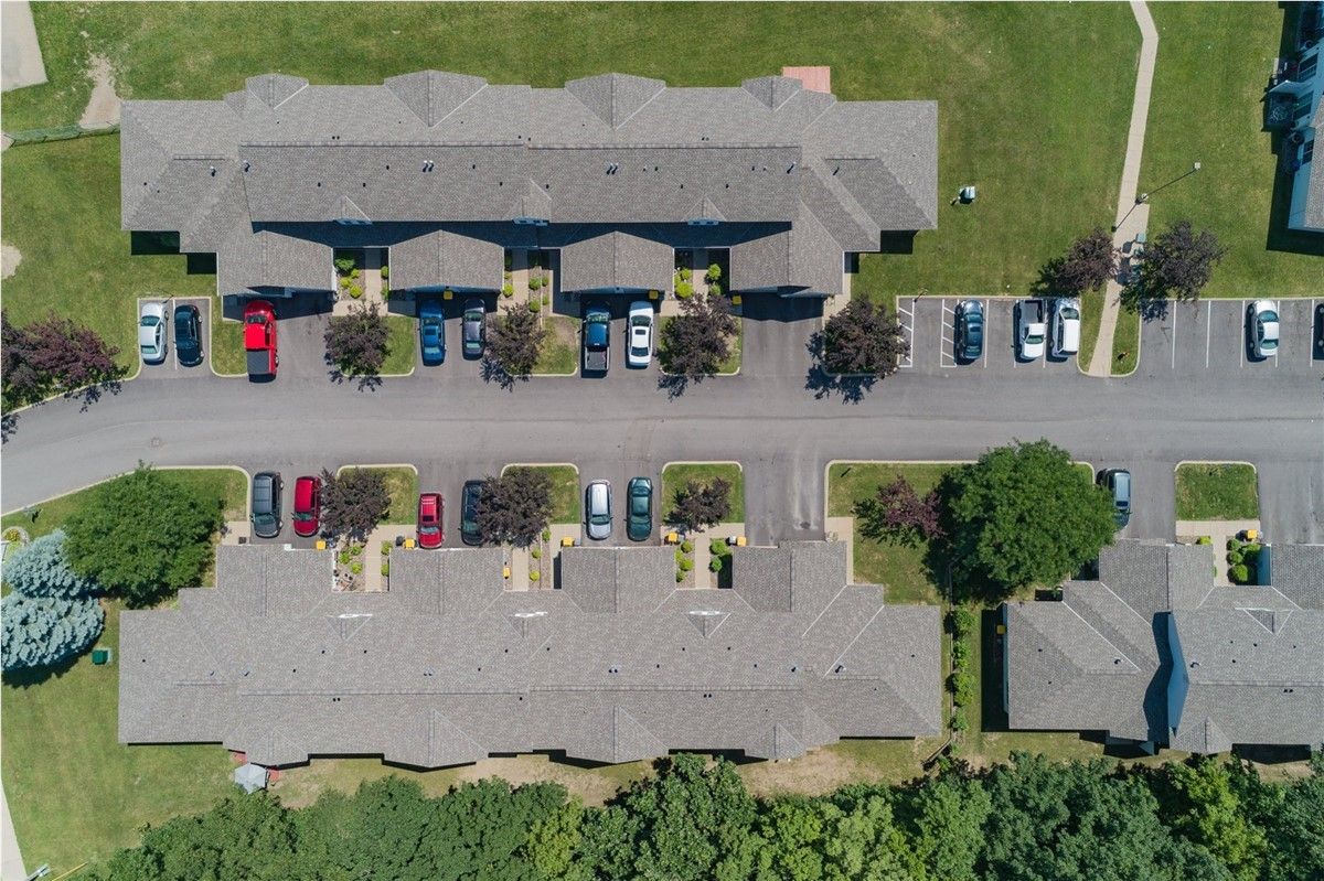 Aerial view of apartment complex with parking, trees, and green lawns. Gray roofs and paved road.
