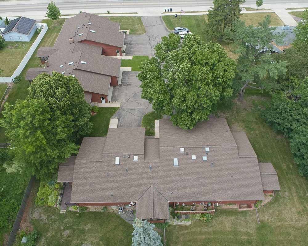 Aerial view of brown-roofed buildings, a road, and green trees on a lawn.