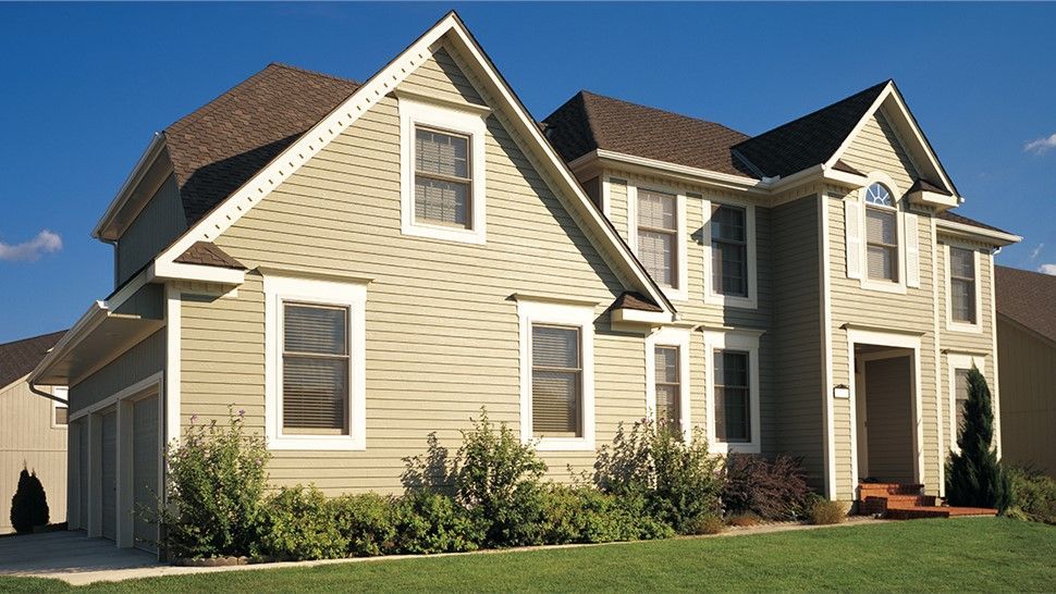Two-story house with green siding, brown roof, and garage, under a blue sky.