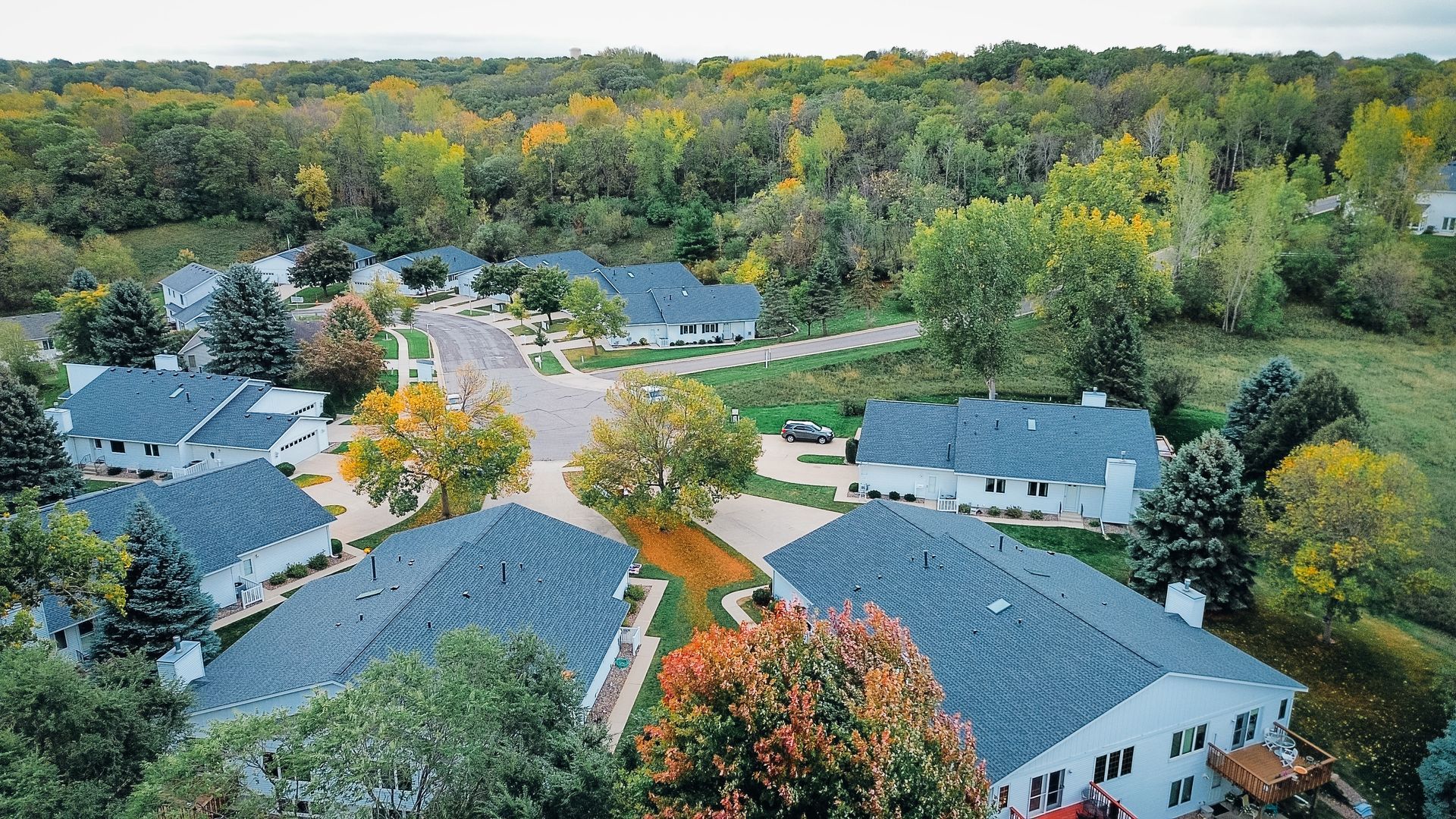 Aerial view of houses with dark roofs surrounded by trees, in an autumn setting.