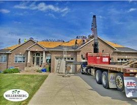 Roofers on a house with a crane. Truck with supplies in driveway. Sunny, blue sky.
