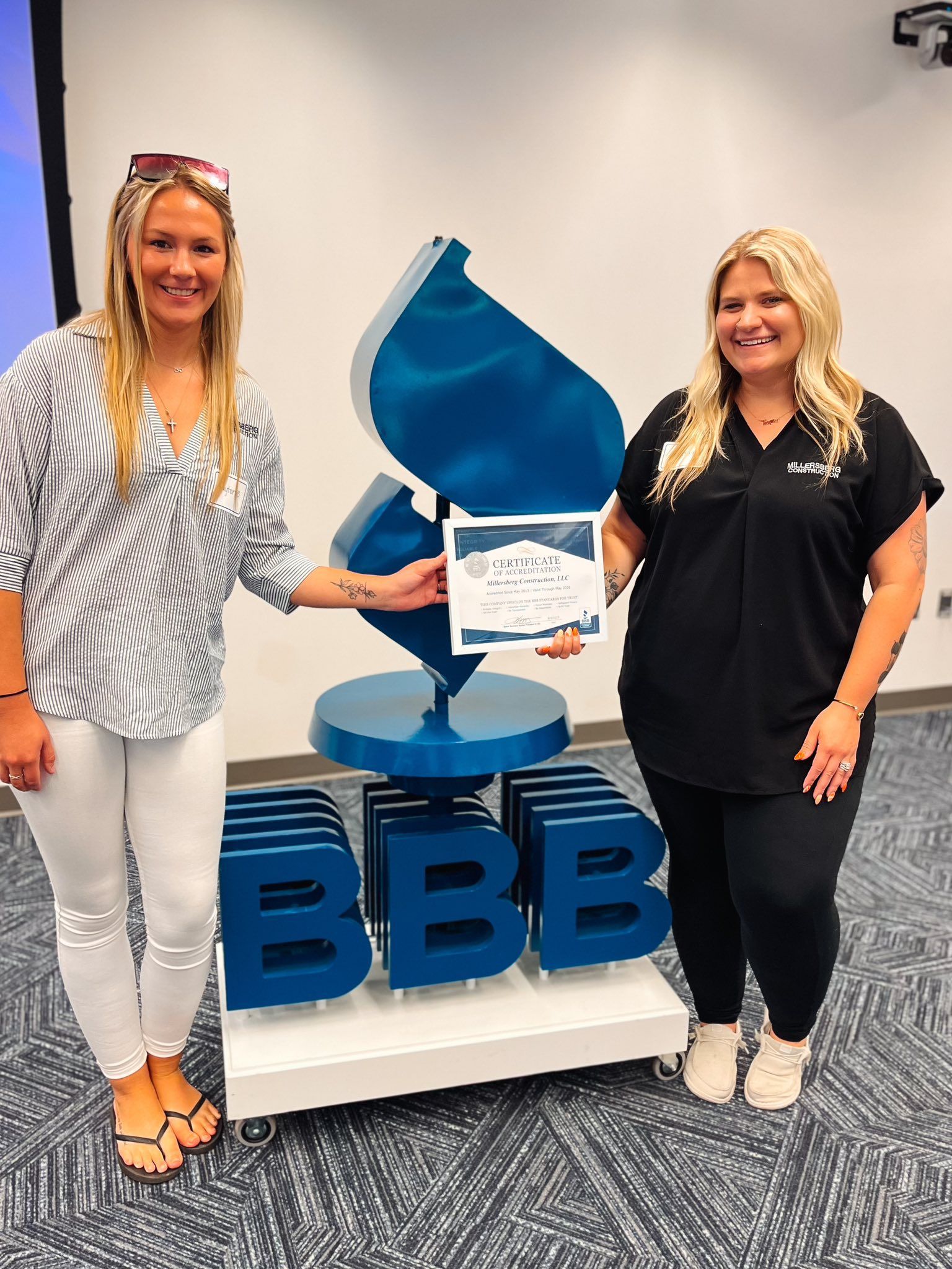Two women stand with a blue BBB logo and award, smiling. One holds the certificate.