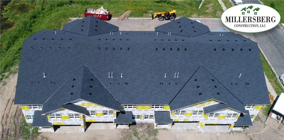 Aerial view of a multi-unit residential building with a dark gray shingled roof, under construction.
