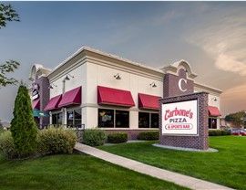 Exterior of Carbone's Pizza & Sports Bar restaurant with red awnings, a sign, and landscaping.