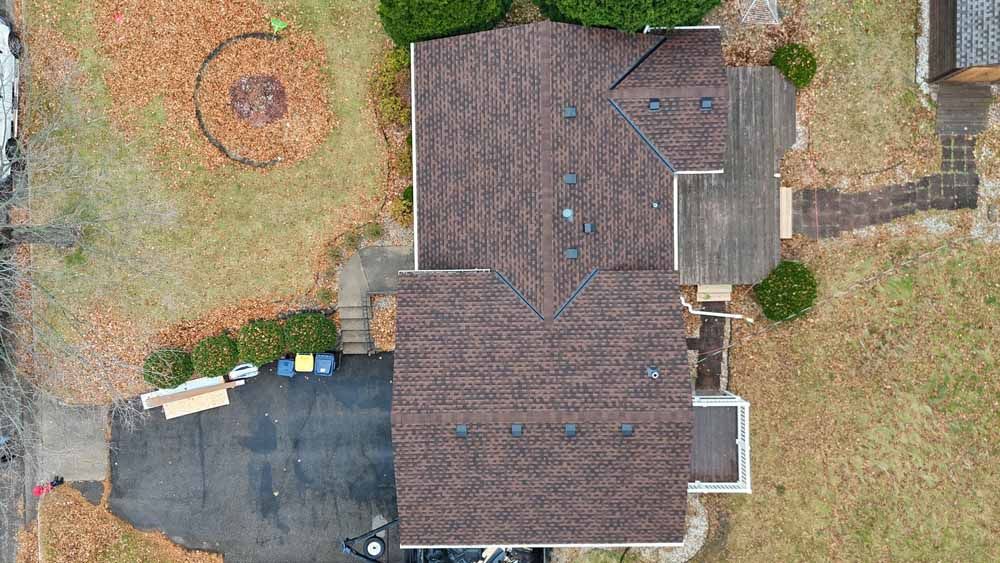 Overhead view of a house with a brown roof and surrounding yard, driveway, and autumn foliage.