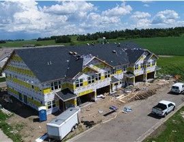 Townhouses under construction, exterior view; yellow wrap, dark roof, vehicles, and trailer.