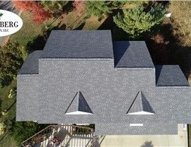 Overhead view of a house with a gray shingle roof, two dormers, and a small deck. Trees surround.