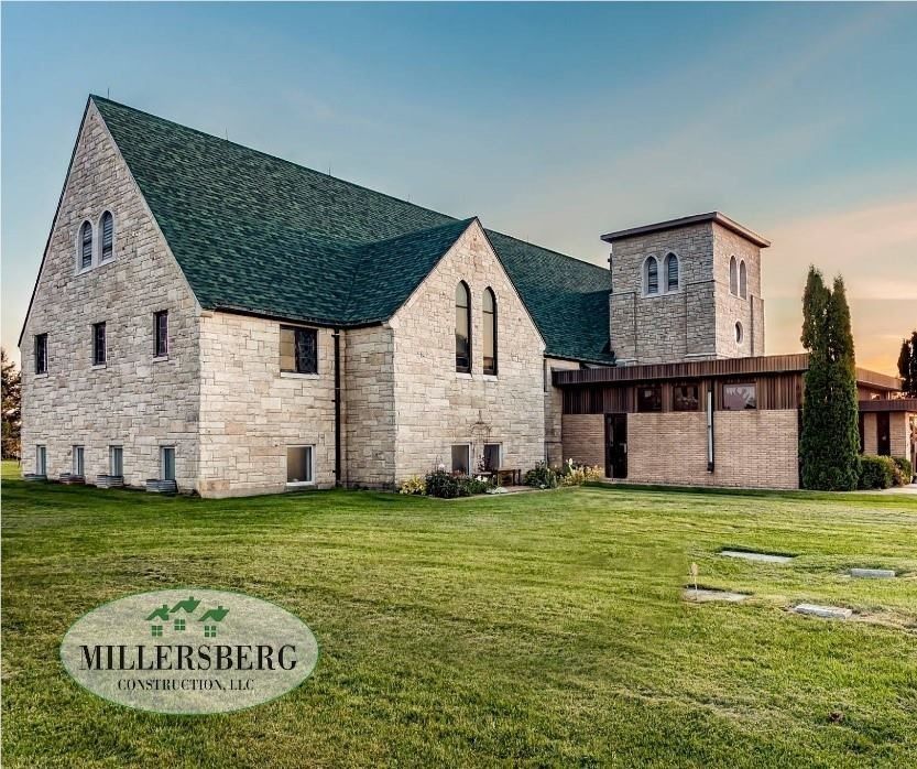 Stone church with green roof and tower on a grassy lawn under a blue sky.