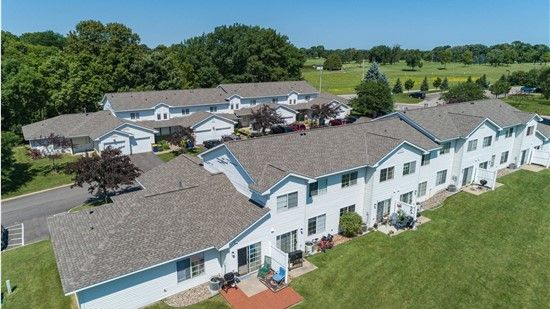 Aerial view of white townhouses with brown roofs and green lawn, golf course in the background.
