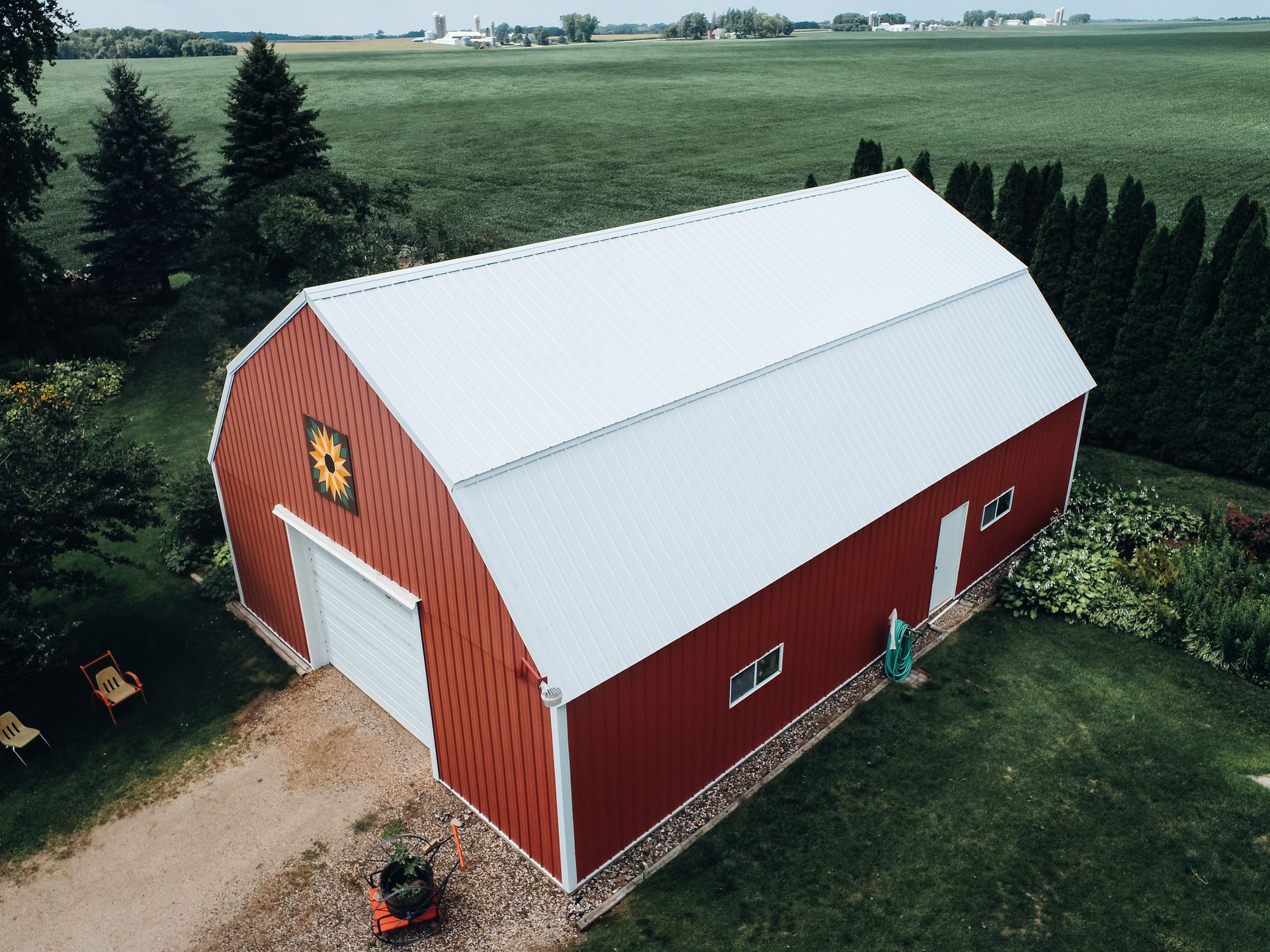 Red barn with white roof, sunflower design, on a grassy plot with a green field background.