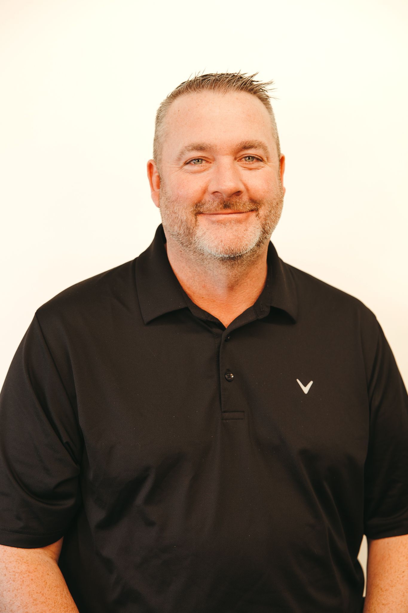 Man in a black polo shirt, smiling, against a light background.