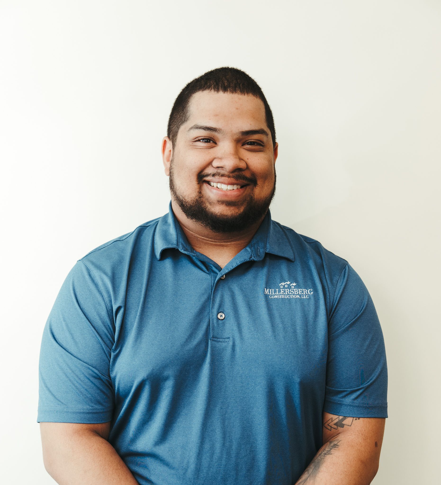 Man in blue polo shirt smiling, standing against a white wall.