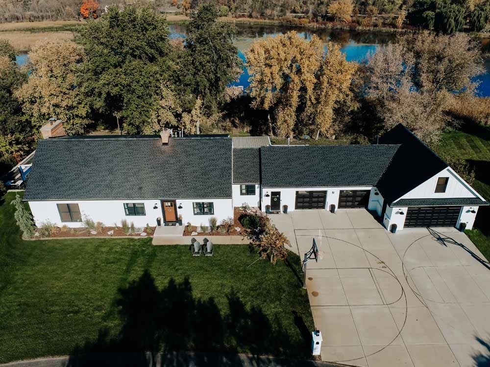 White house with black roof and garage, overlooking a river with fall foliage.