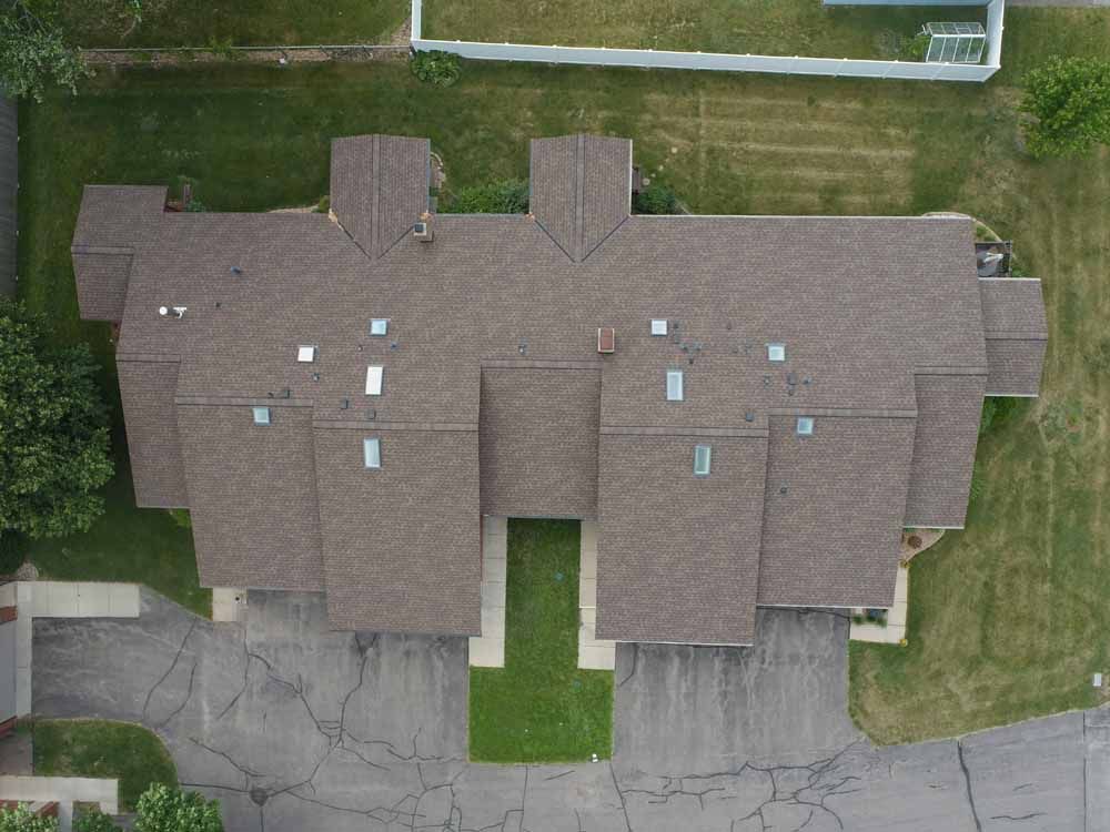 Overhead view of a brown-roofed building with multiple sections, driveways, and surrounding green grass.