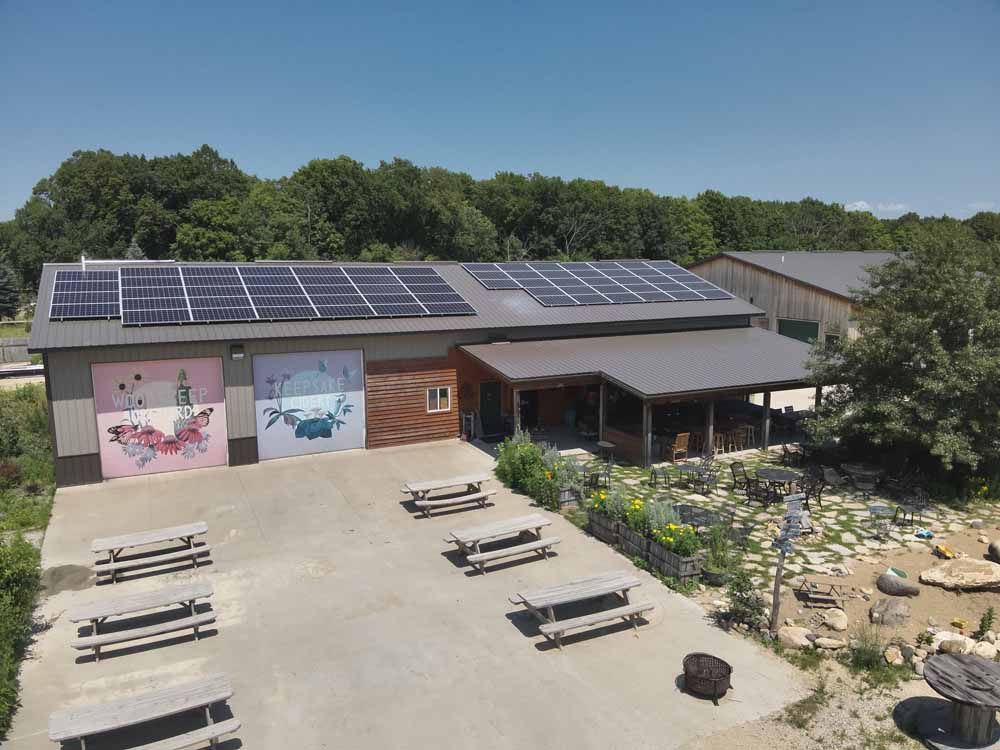 Building with solar panels, murals, picnic tables, and garden under blue sky.