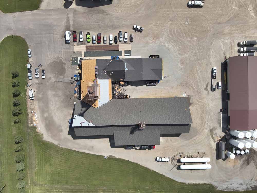 Aerial view of a building with a gray roof and several vehicles parked around it on a gravel lot.