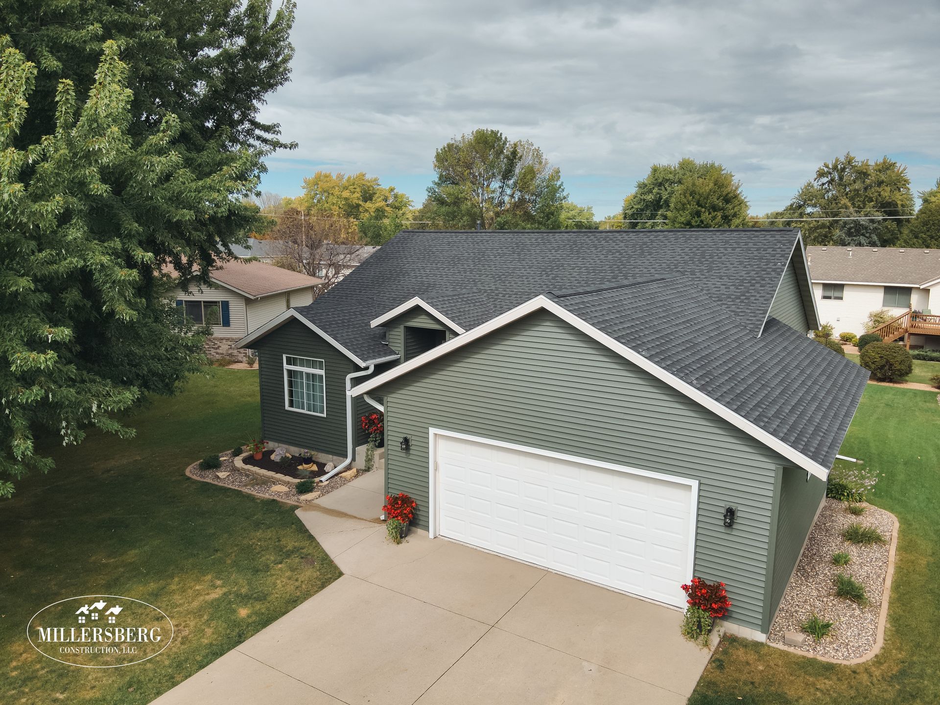 Green house with white garage door and dark gray roof on a cloudy day.