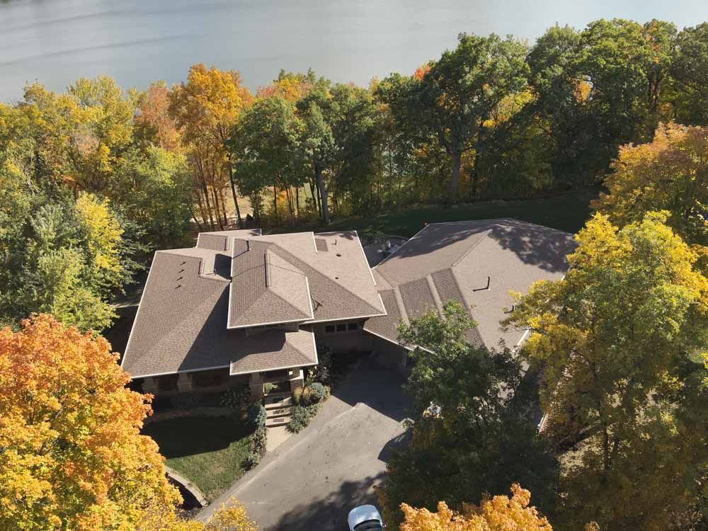 House surrounded by autumn trees, with a driveway and view of a body of water in the distance.