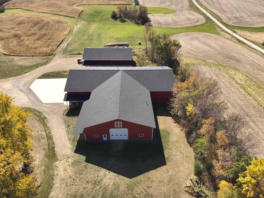Red barn with gray roof on a rural property, surrounded by fields and a gravel driveway.