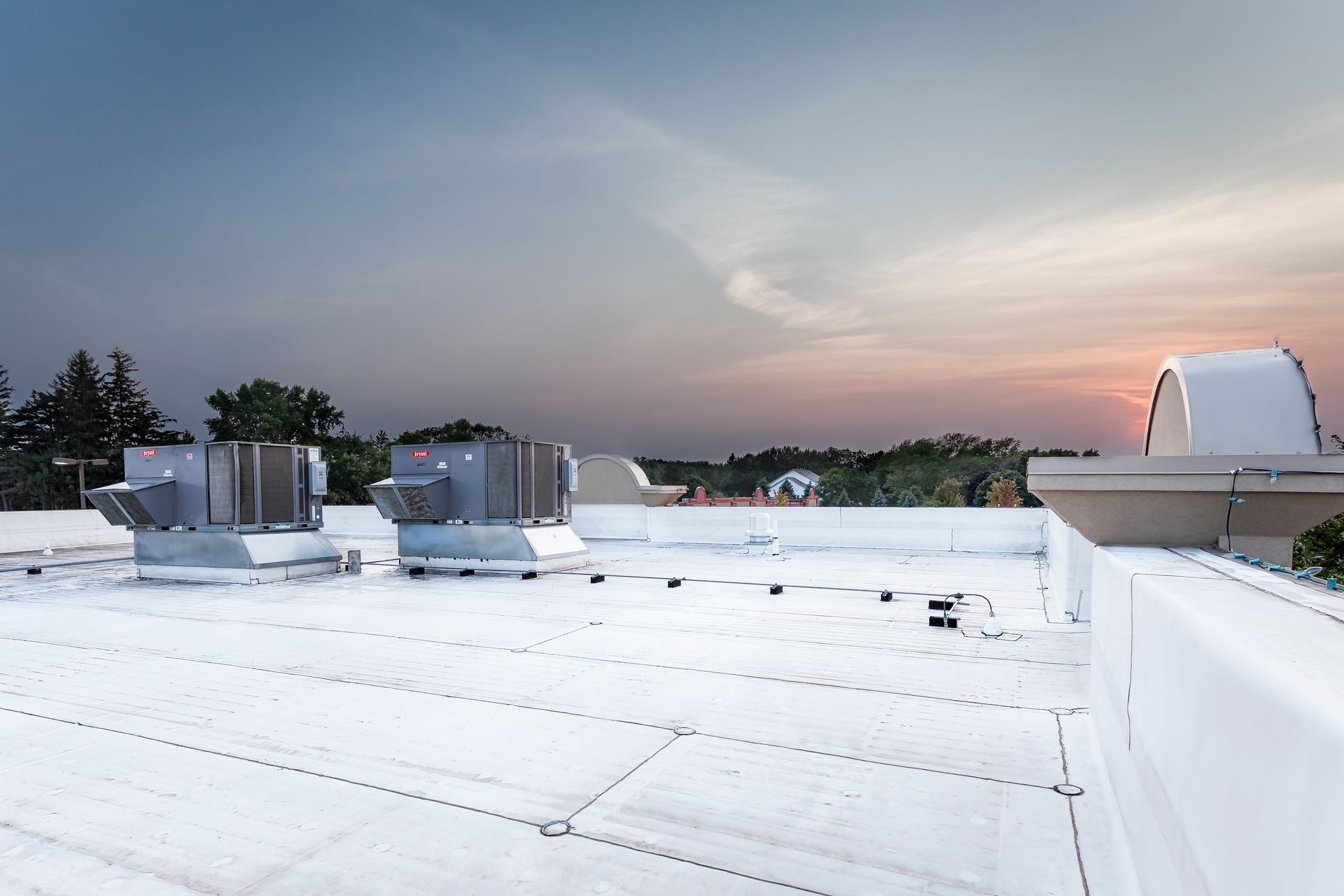 White rooftop with air conditioning units against a colorful sunset.