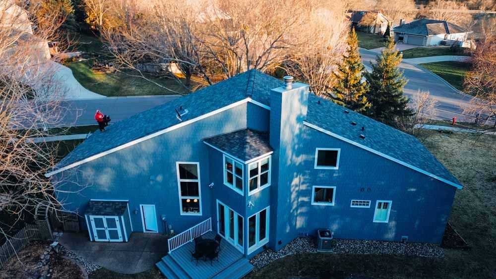 Blue house with multiple windows and a gray roof, in a residential area.