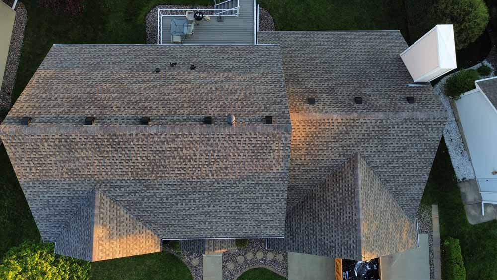 Overhead view of a house with a gray shingled roof, ventilation pipes, and a white satellite dish.