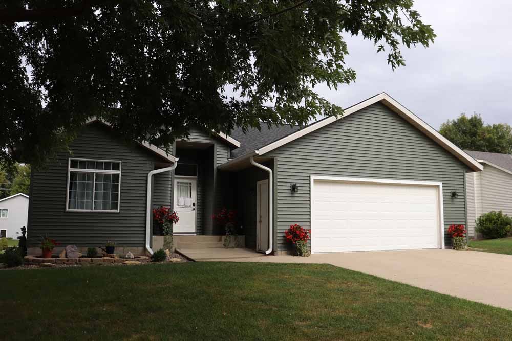 Green-sided house with a white garage door, front porch, and steps, with a tree in front.