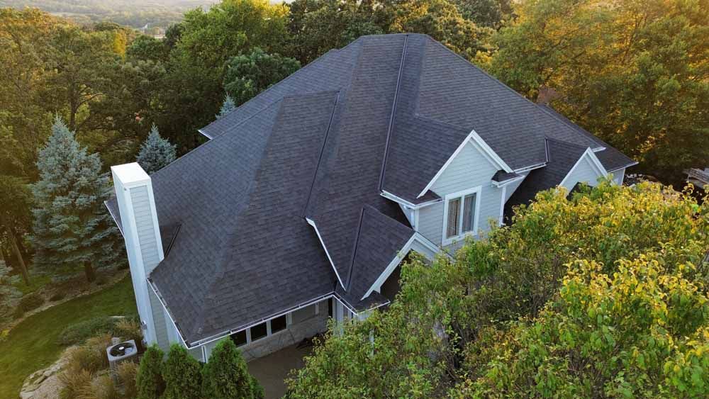 Gray house with dark roof surrounded by trees.