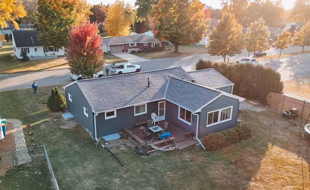 Aerial view of a gray house with a newly shingled roof and colorful fall trees.
