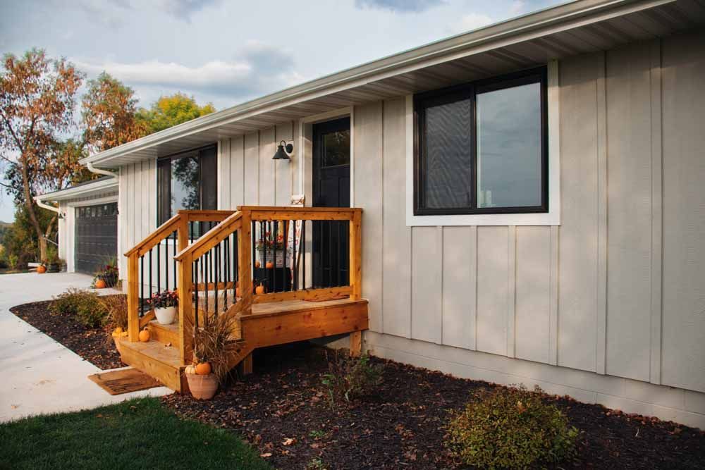 Exterior of a light gray house with black windows and wooden porch.