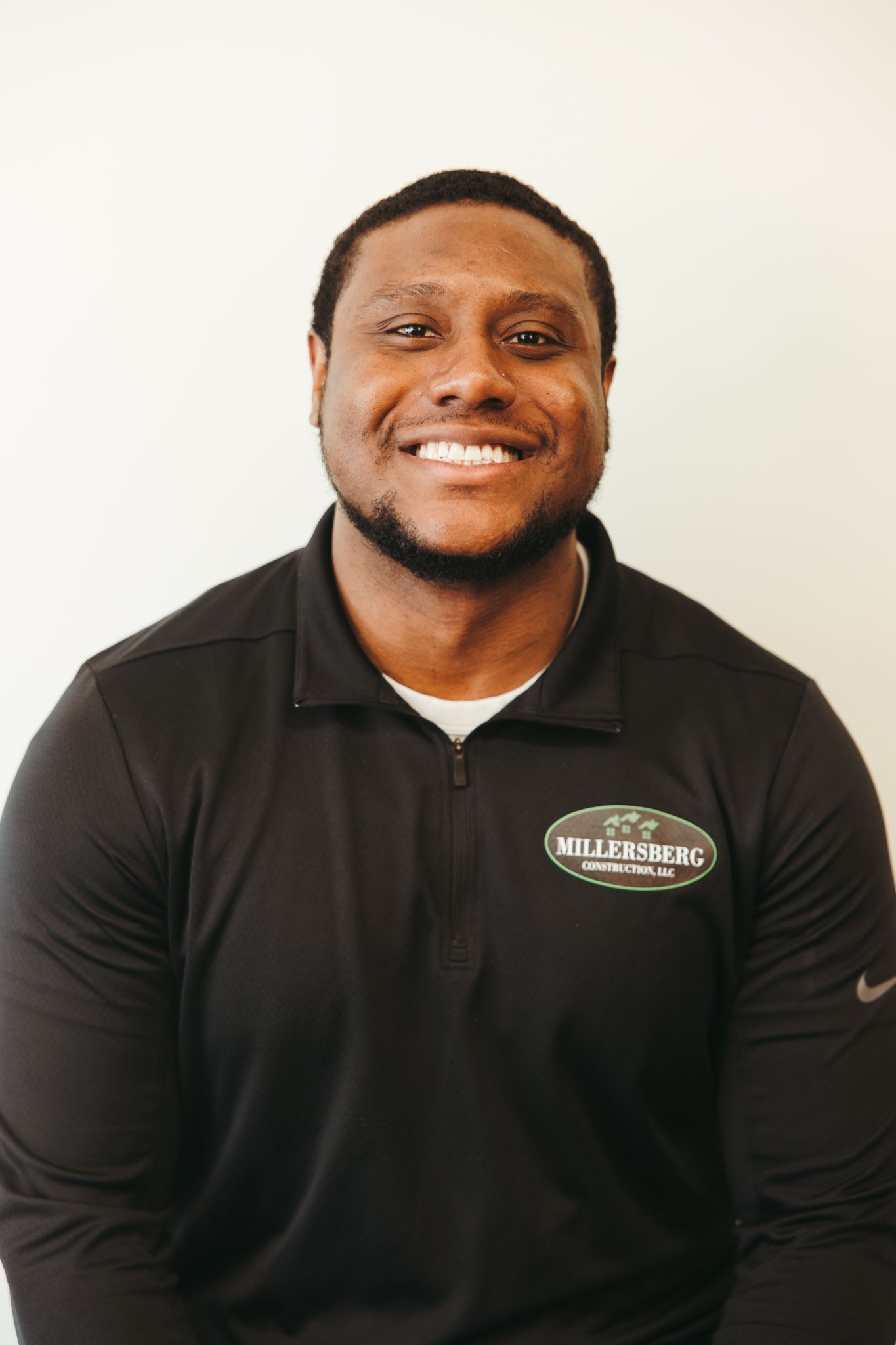 Man smiling in a black polo shirt, with a logo and a white collared undershirt, against a plain background.