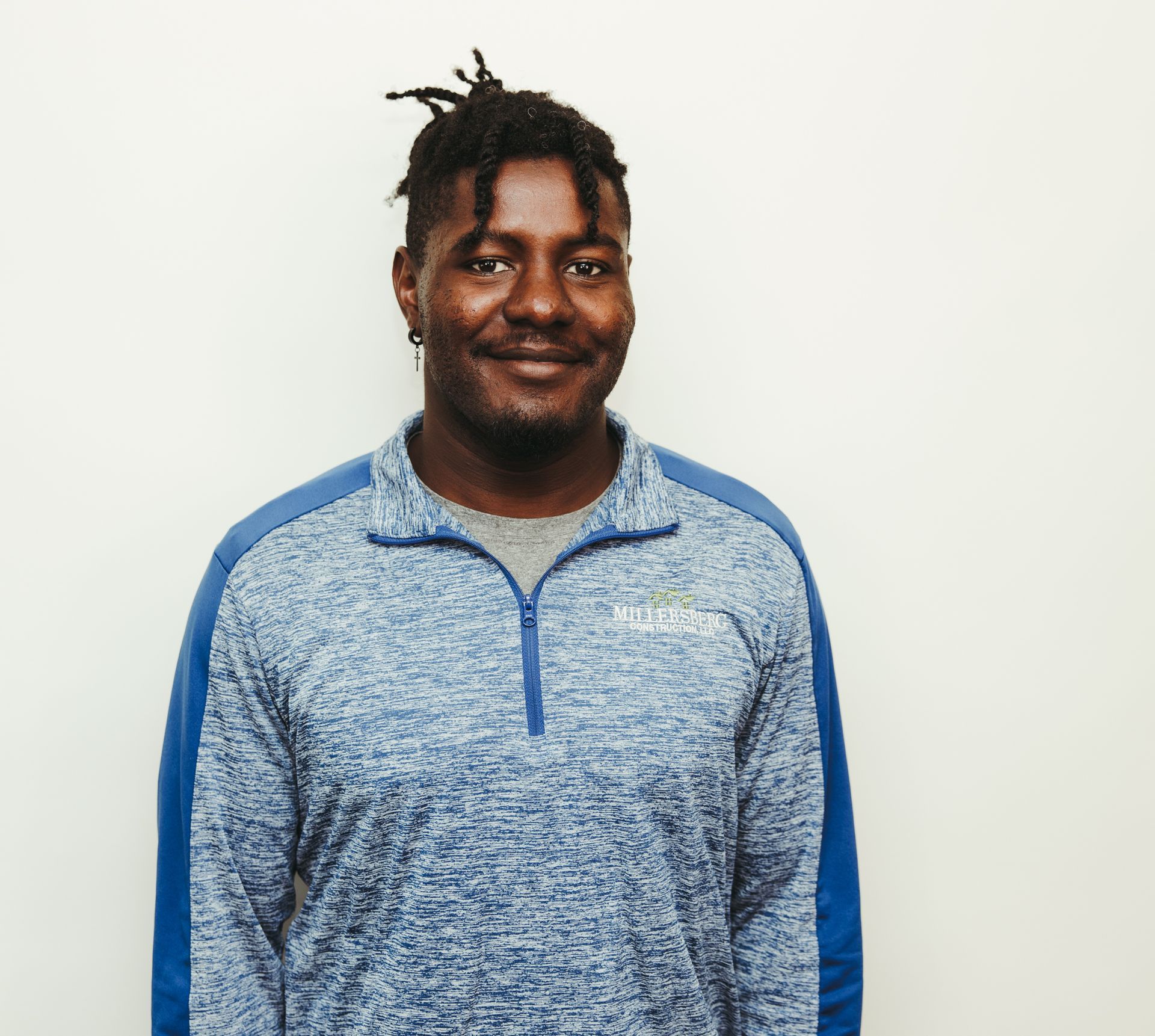Man with dreadlocks smiling, wearing a blue and gray zip-up sweater.
