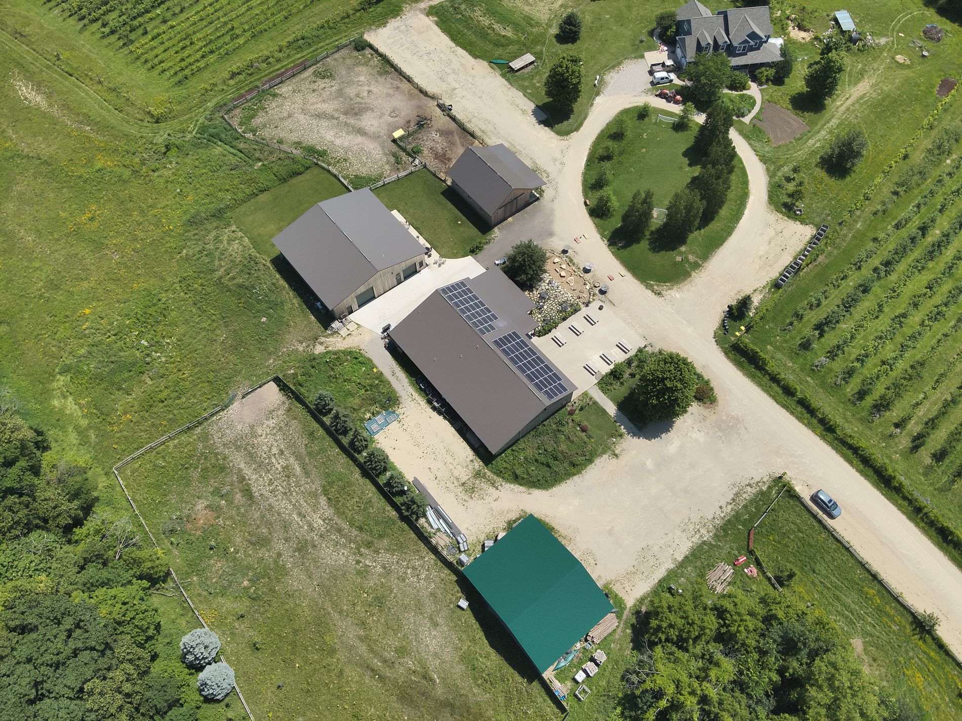 Aerial view of buildings, gravel roads, green fields, and a vineyard.