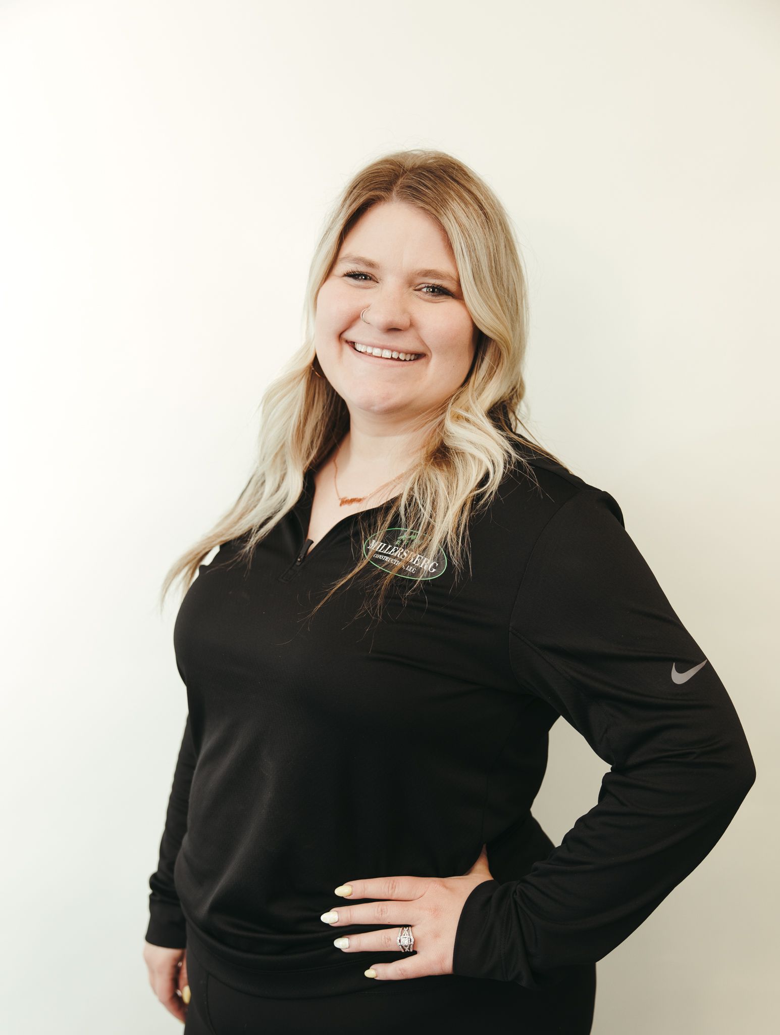 Woman with long blonde hair, smiling, wearing a black shirt, posing against a white background.