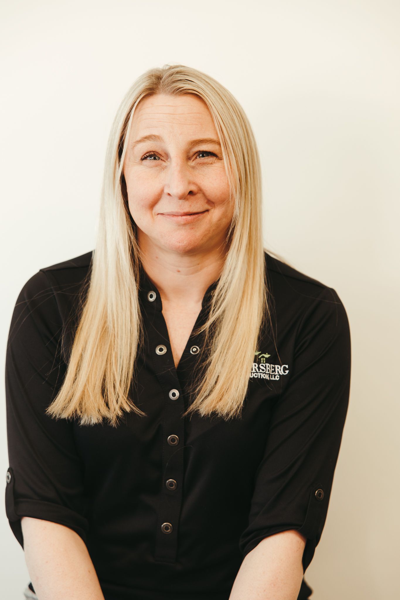 Woman with blonde hair wearing a black shirt, smiling in front of a white wall.