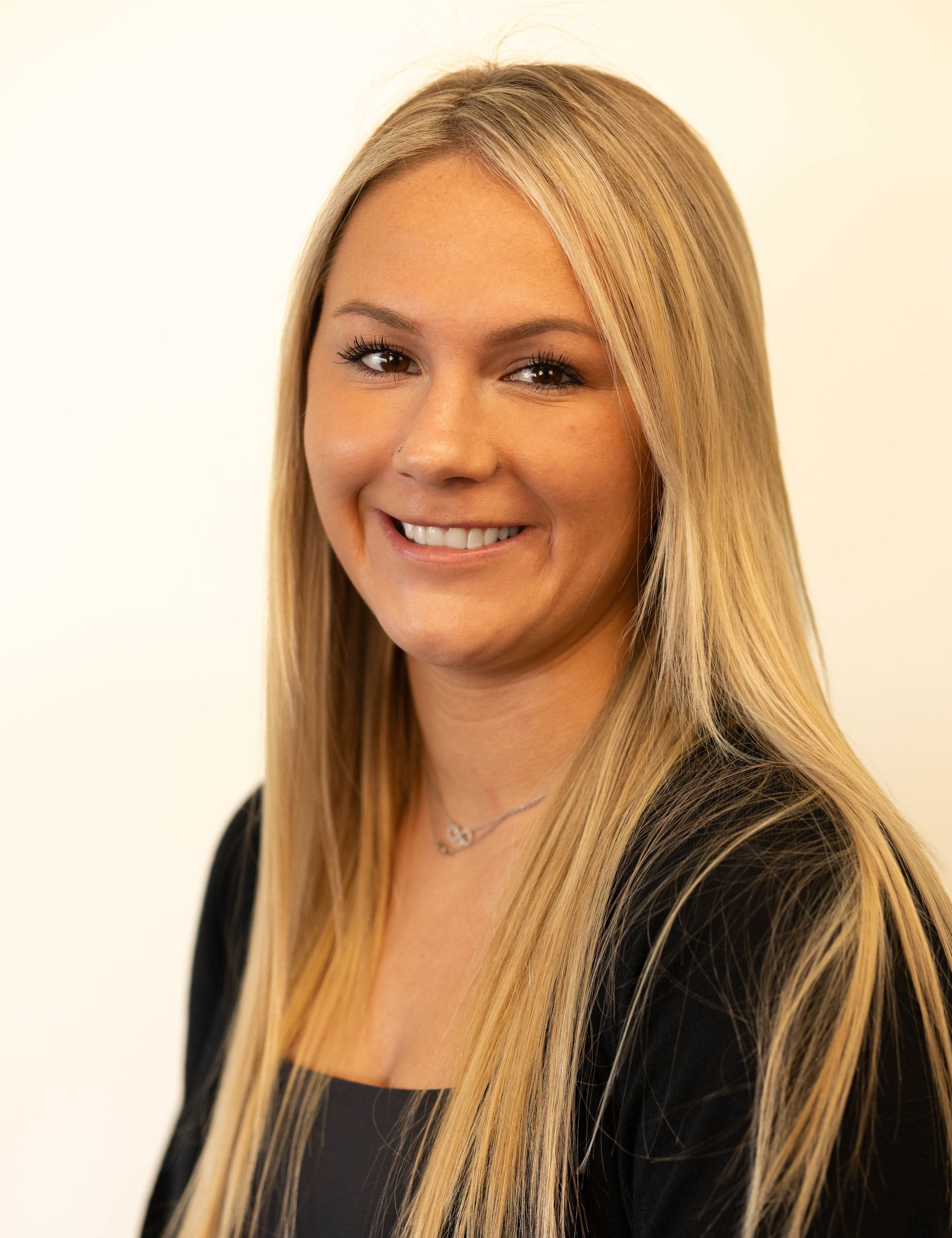 Woman with long blonde hair, smiling at camera, wearing a black top.