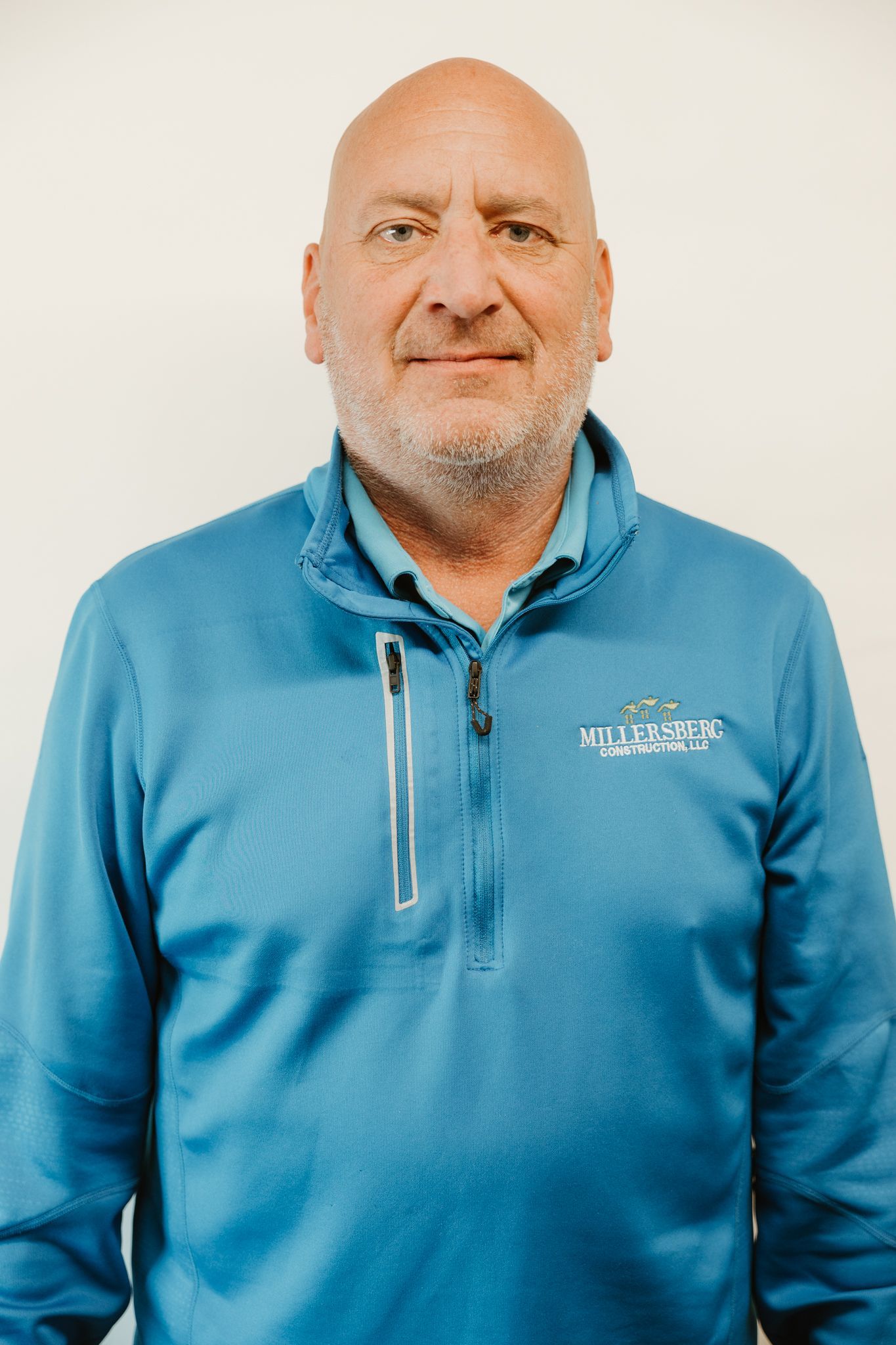 A bald man wearing a blue jacket smiles slightly. White background.