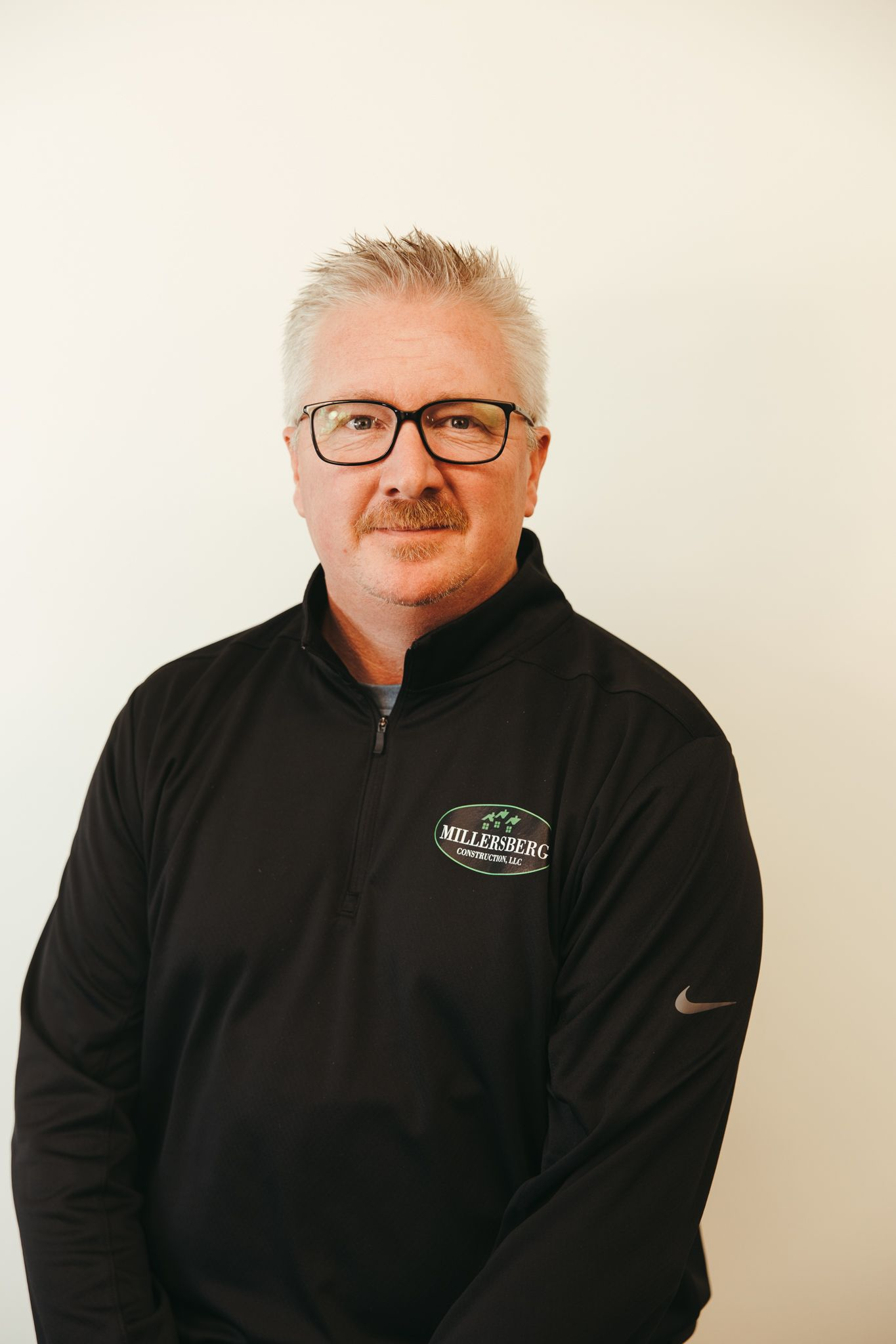 Man with glasses wearing a black jacket, smiling. Against a white background.