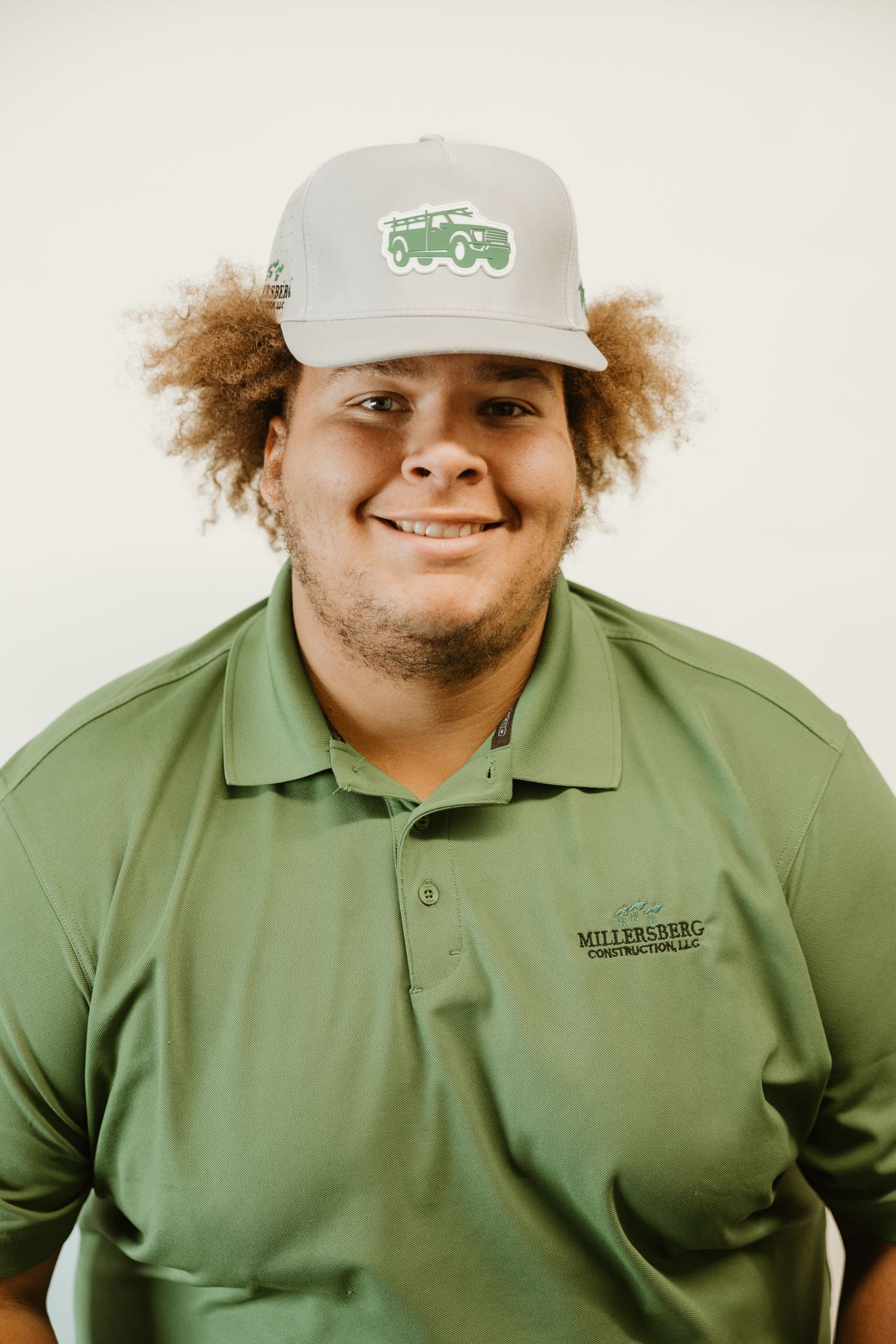 Man wearing a green shirt and a gray hat with green lettering, smiling.
