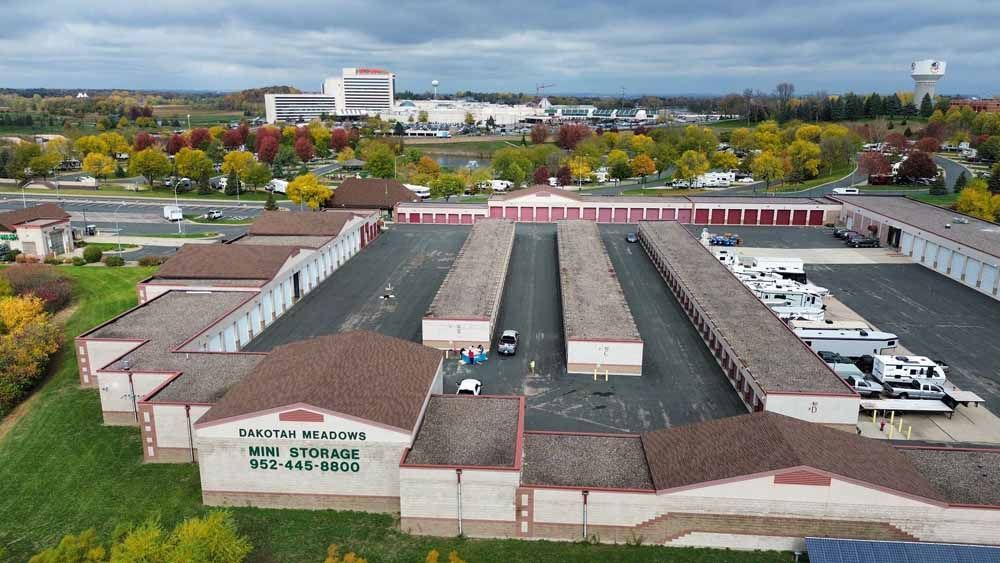 Aerial view of a storage facility with rows of units, brown roofs, and a cityscape in the background.