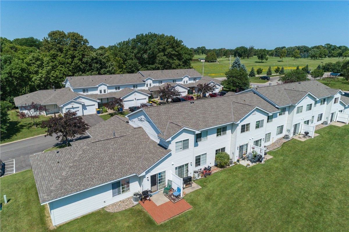 Aerial view of a row of white townhomes with gray roofs and green lawn in a suburban setting.