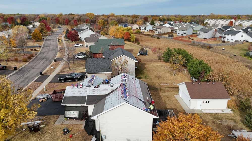 Aerial view of workers replacing a roof on a house in a suburban neighborhood.