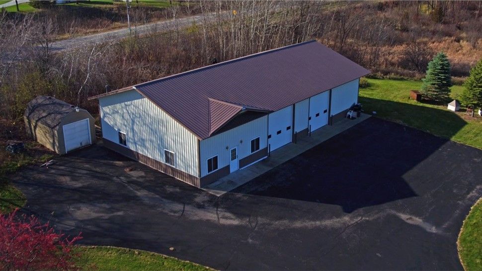 Building with brown roof and garage doors on black asphalt driveway, surrounded by trees.