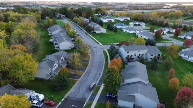 Aerial view of a suburban neighborhood with houses, a curving road, and autumn trees.