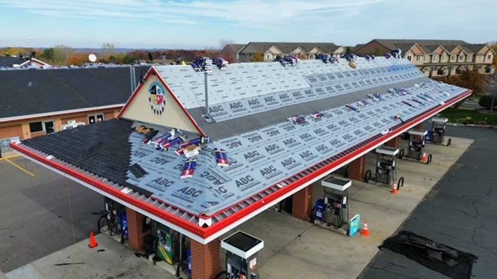Gas station roof under construction. Workers installing roofing material; red and black canopy.