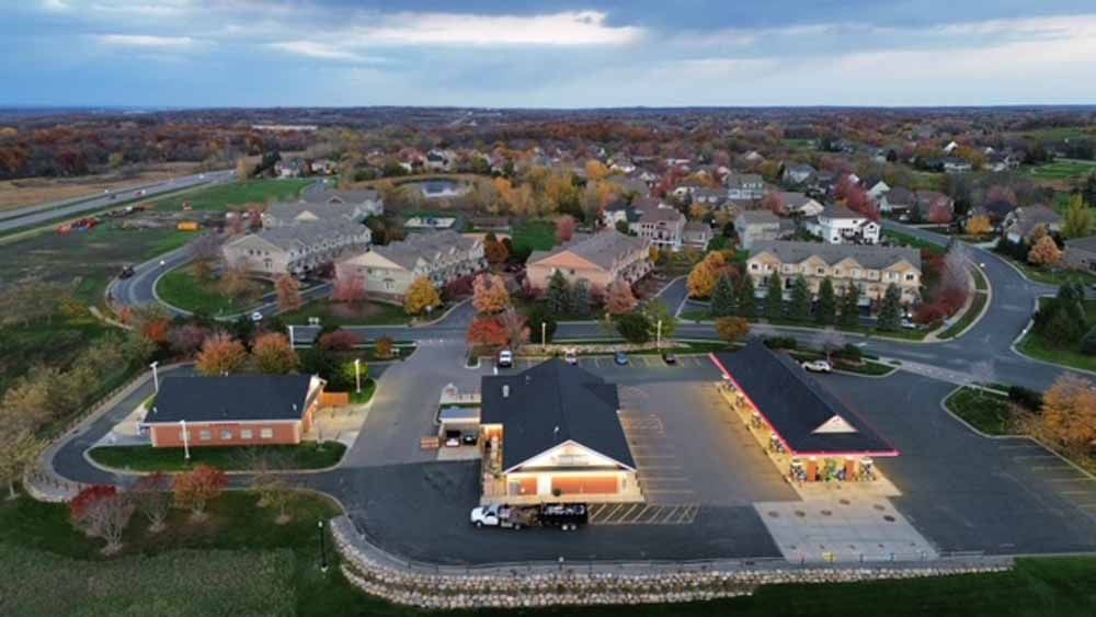 Aerial view of a town with a gas station, buildings, and colorful trees under a cloudy sky.